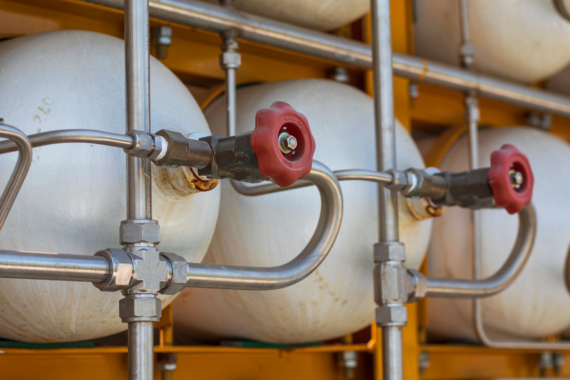Close-up of pressurized gas tanks with red valves and connecting stainless steel pipes.