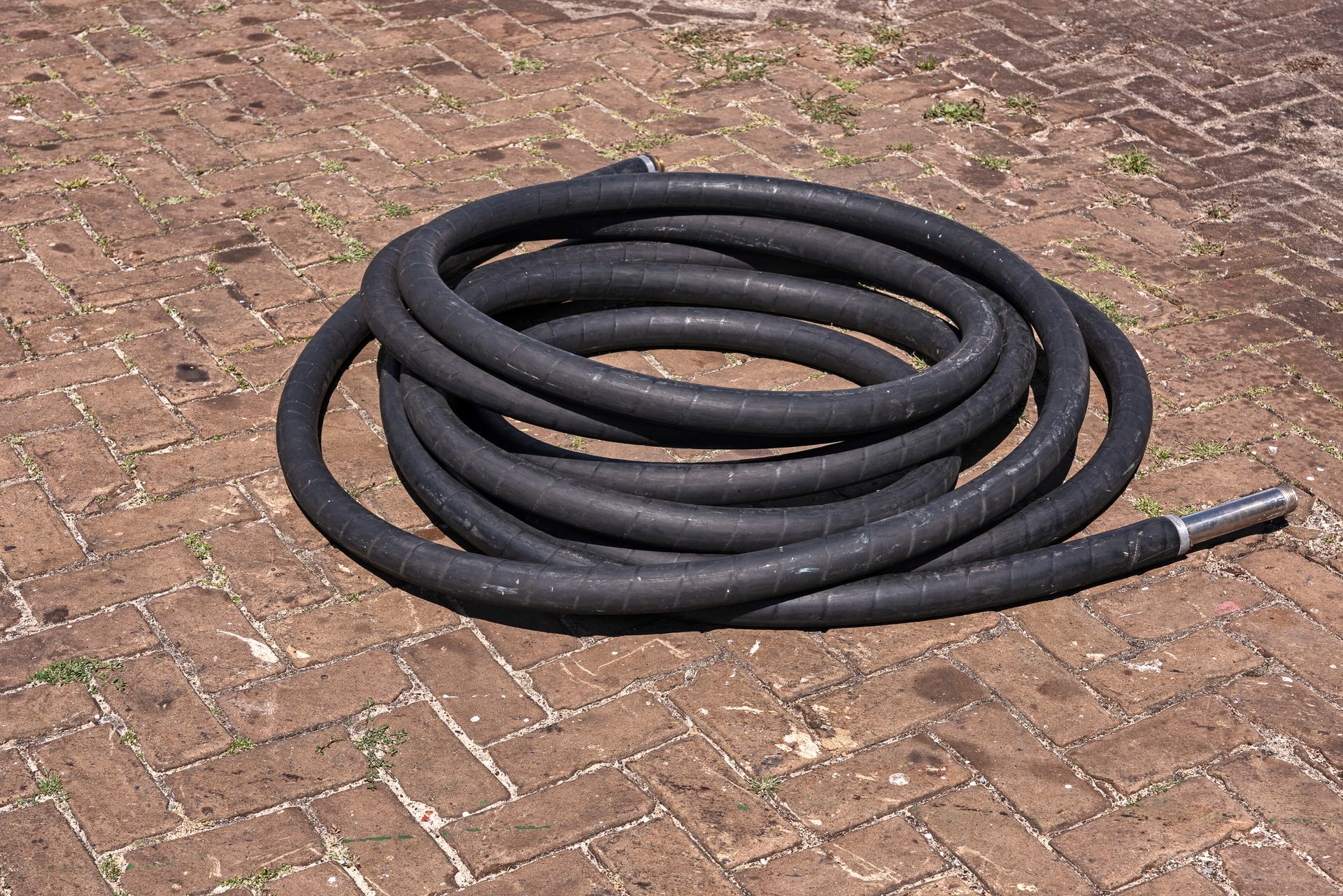 Coiled black hose on a brick patio. One end has a metallic fitting.