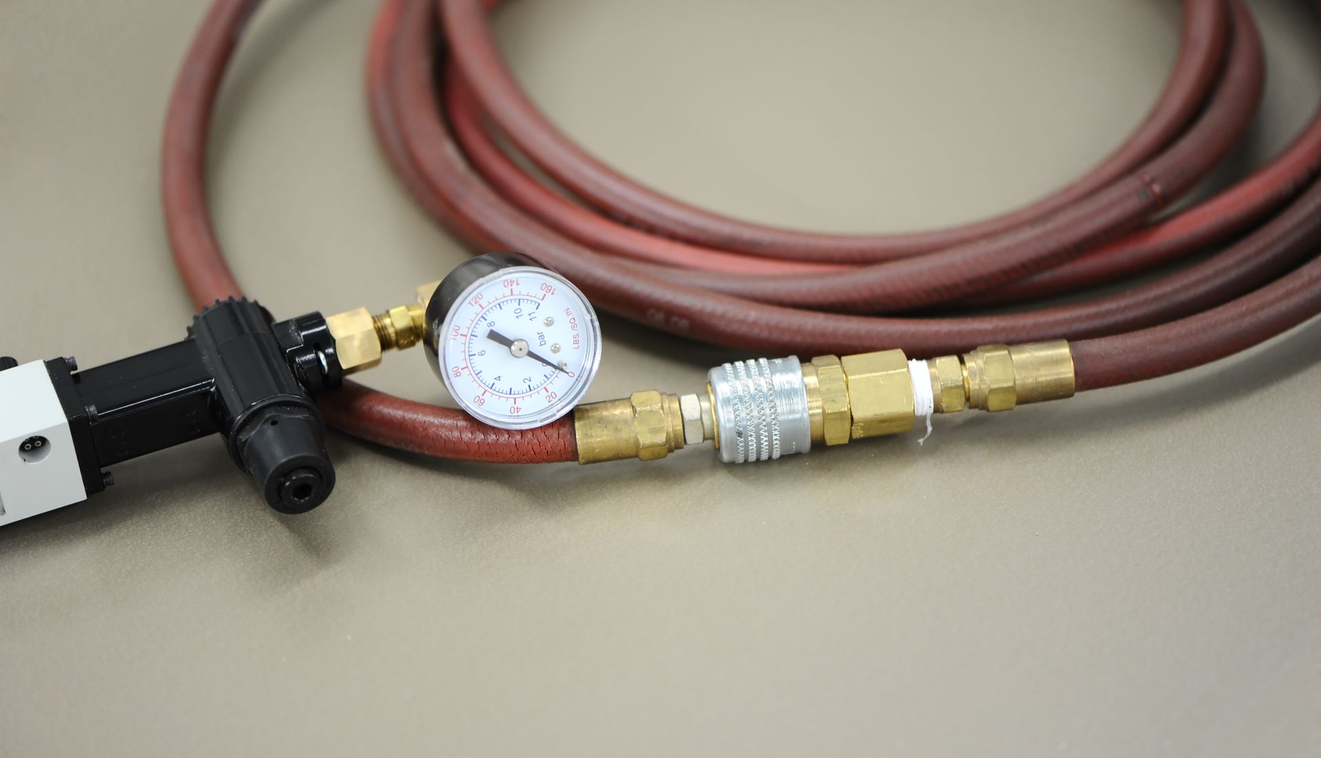 A gauge connected to an air hose coiled on a surface. The gauge has a white face and black needle, indicating pressure.