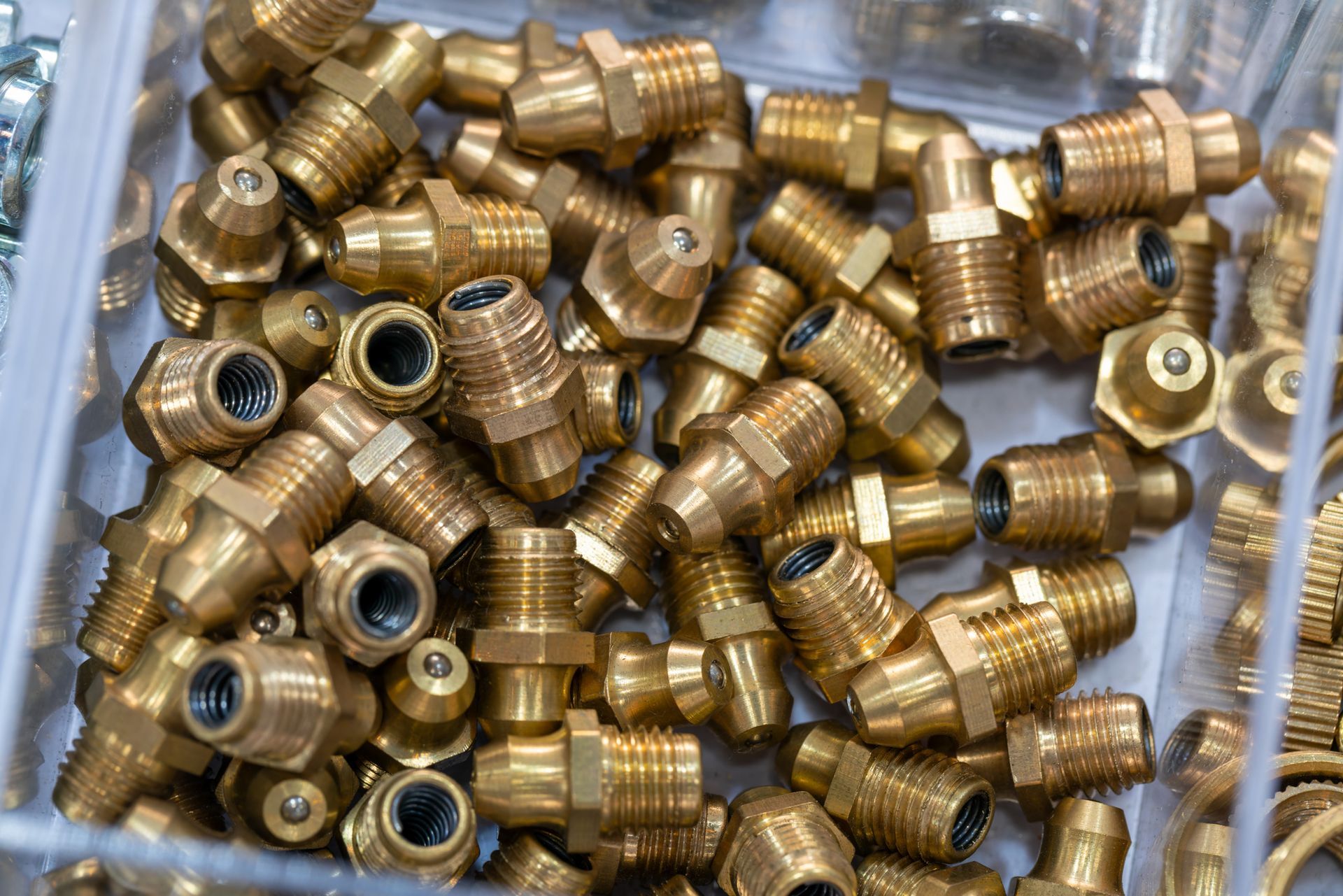 Brass grease fittings in a clear container, various shapes and sizes.