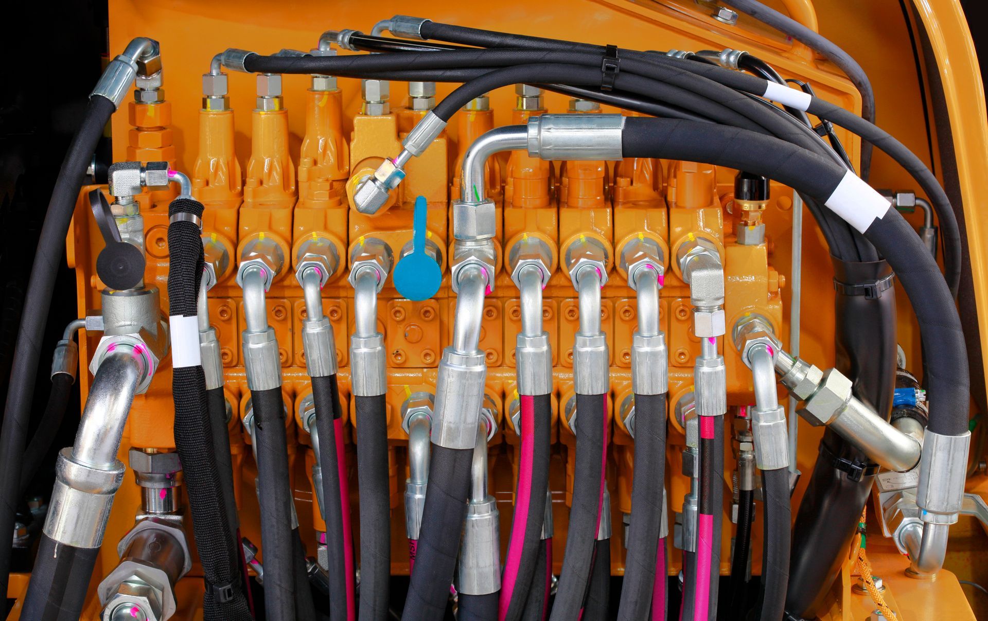 Hydraulic hoses and fittings connected to an orange control valve bank. Hydraulic hoses and fittings connected to an orange control valve bank.
