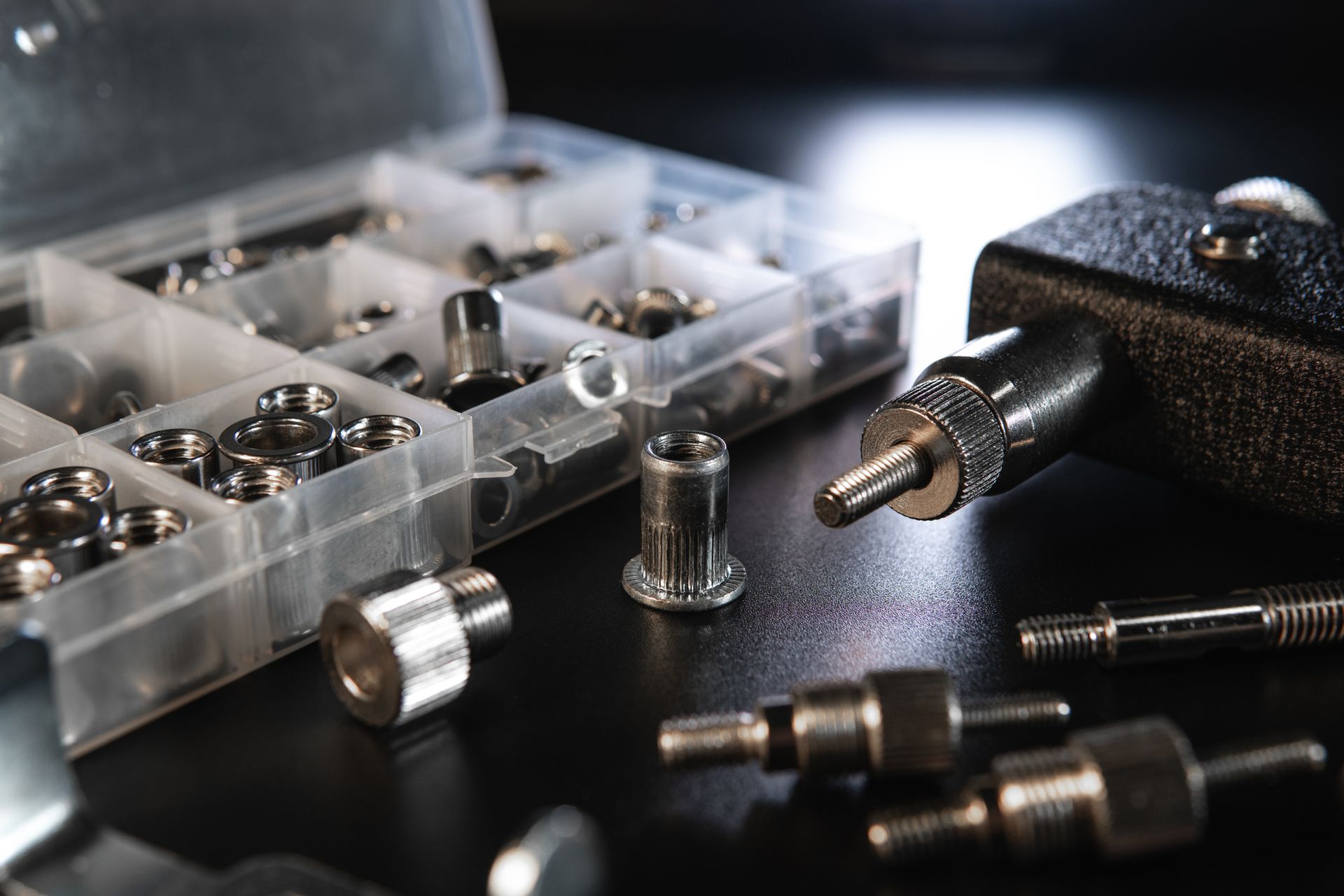 Close-up of a toolbox with various metal rivets and a riveter, on a dark surface.