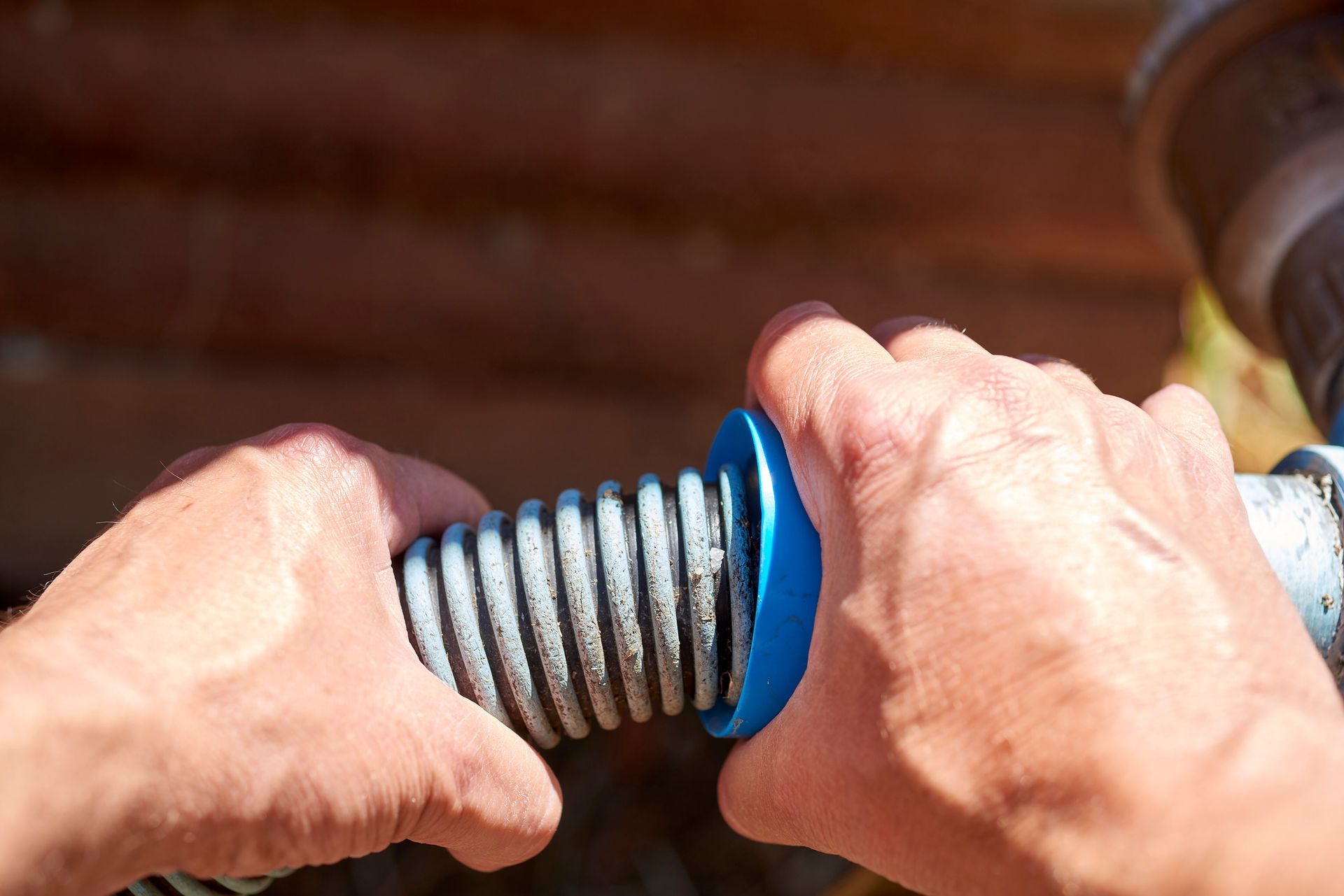 Hands gripping a blue spring with a silver coil, likely for a garage door, against a wooden background.