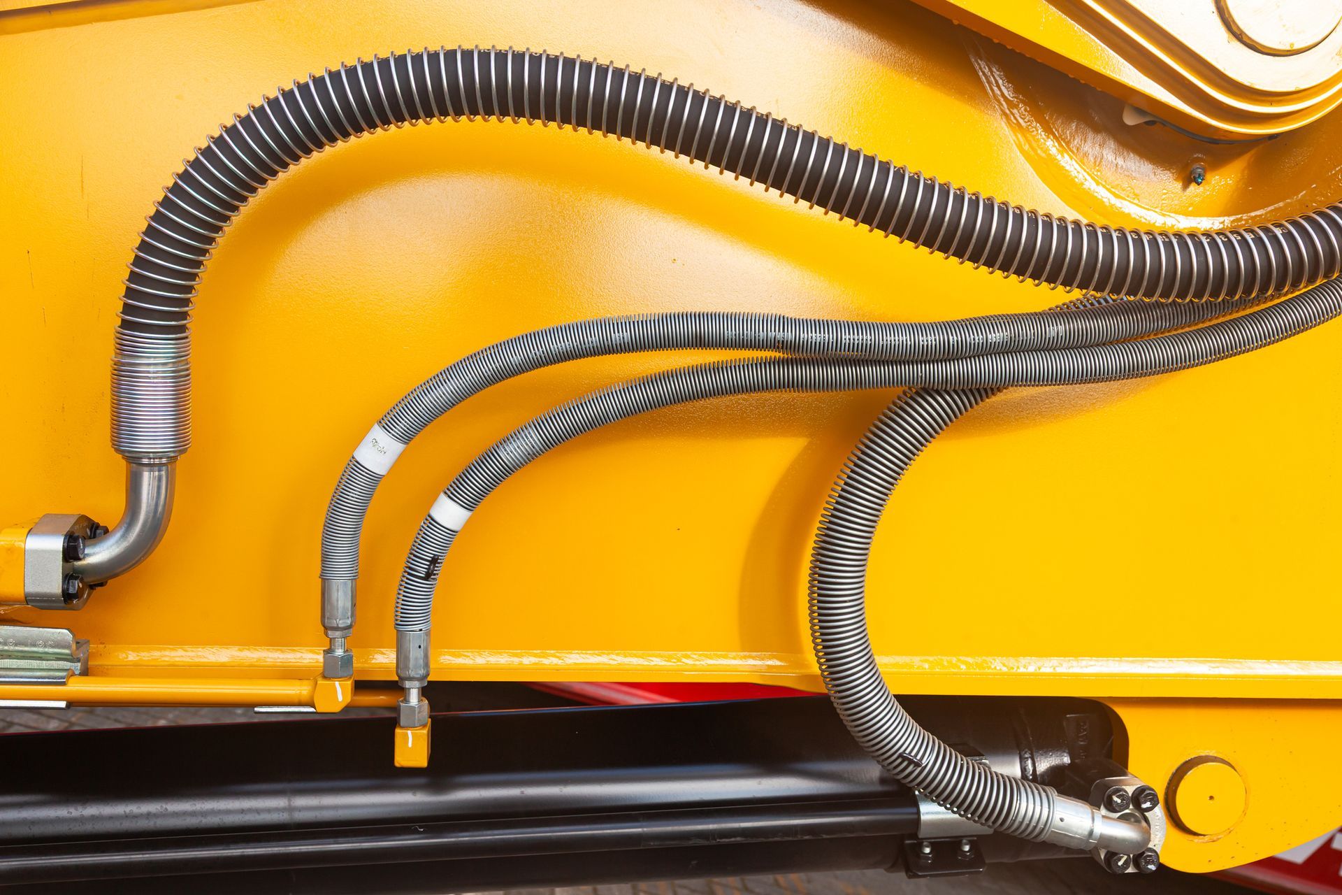 Yellow industrial machinery with black and grey hydraulic hoses.