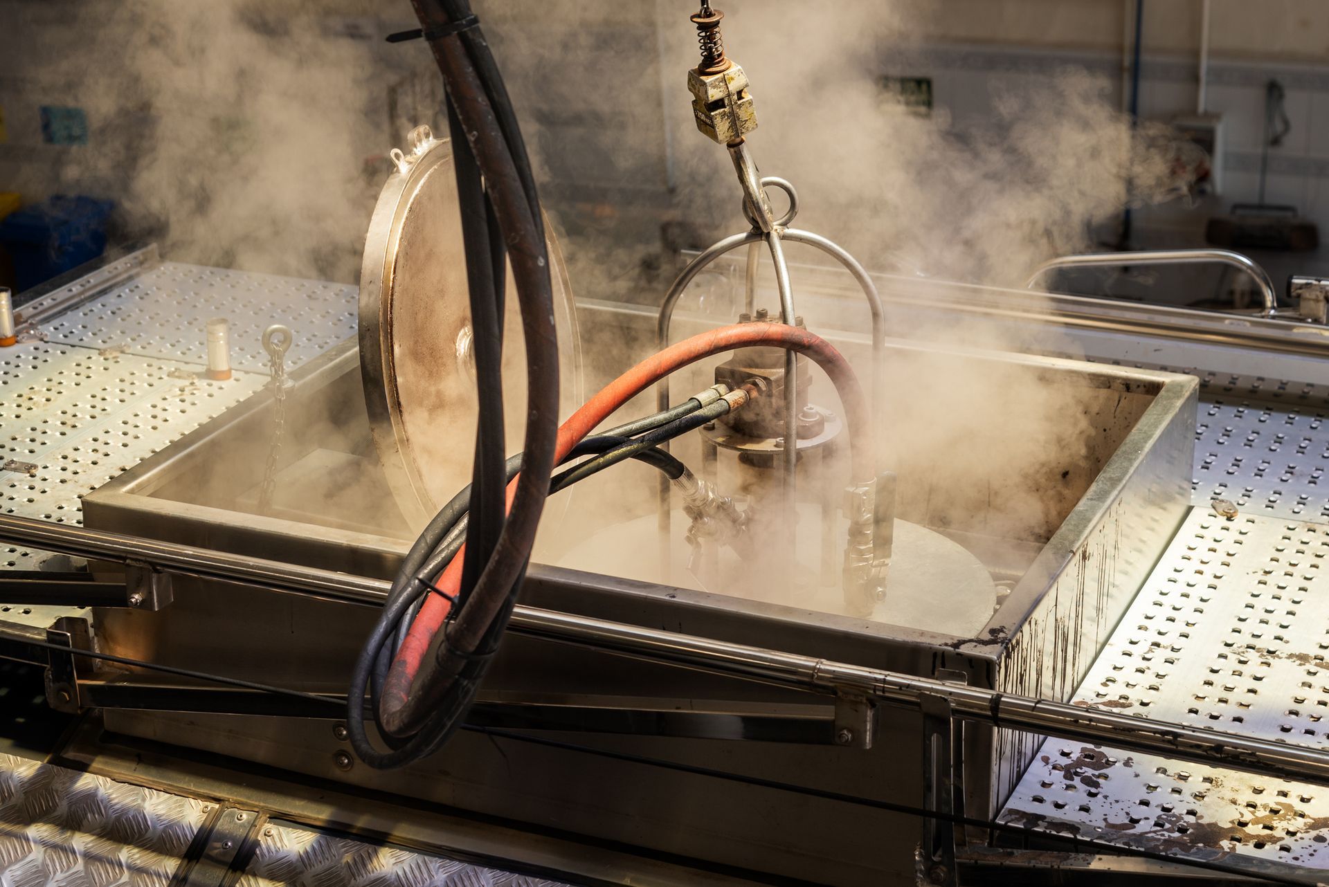 A steaming metal tub with tools submerged, generating a cloud of steam in a factory setting.