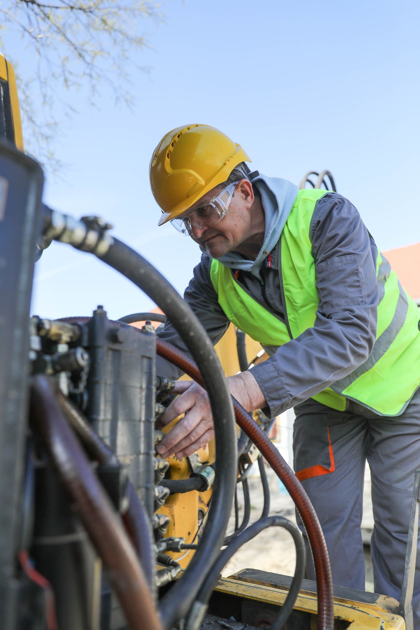 A male technician wearing a work uniform repairs hydraulic components on construction machinery A male technician wearing a work uniform repairs hydraulic components on construction machinery