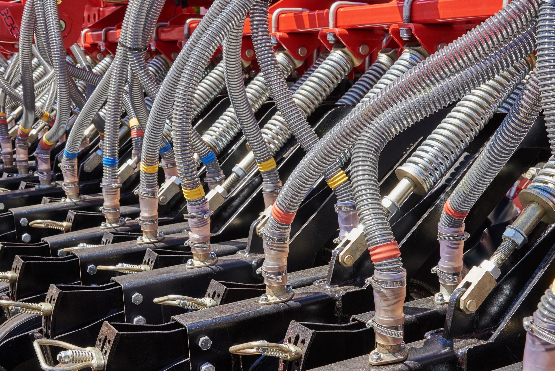 Close-up of farm machinery showing multiple flexible tubes with colorful connectors and black metal components.
