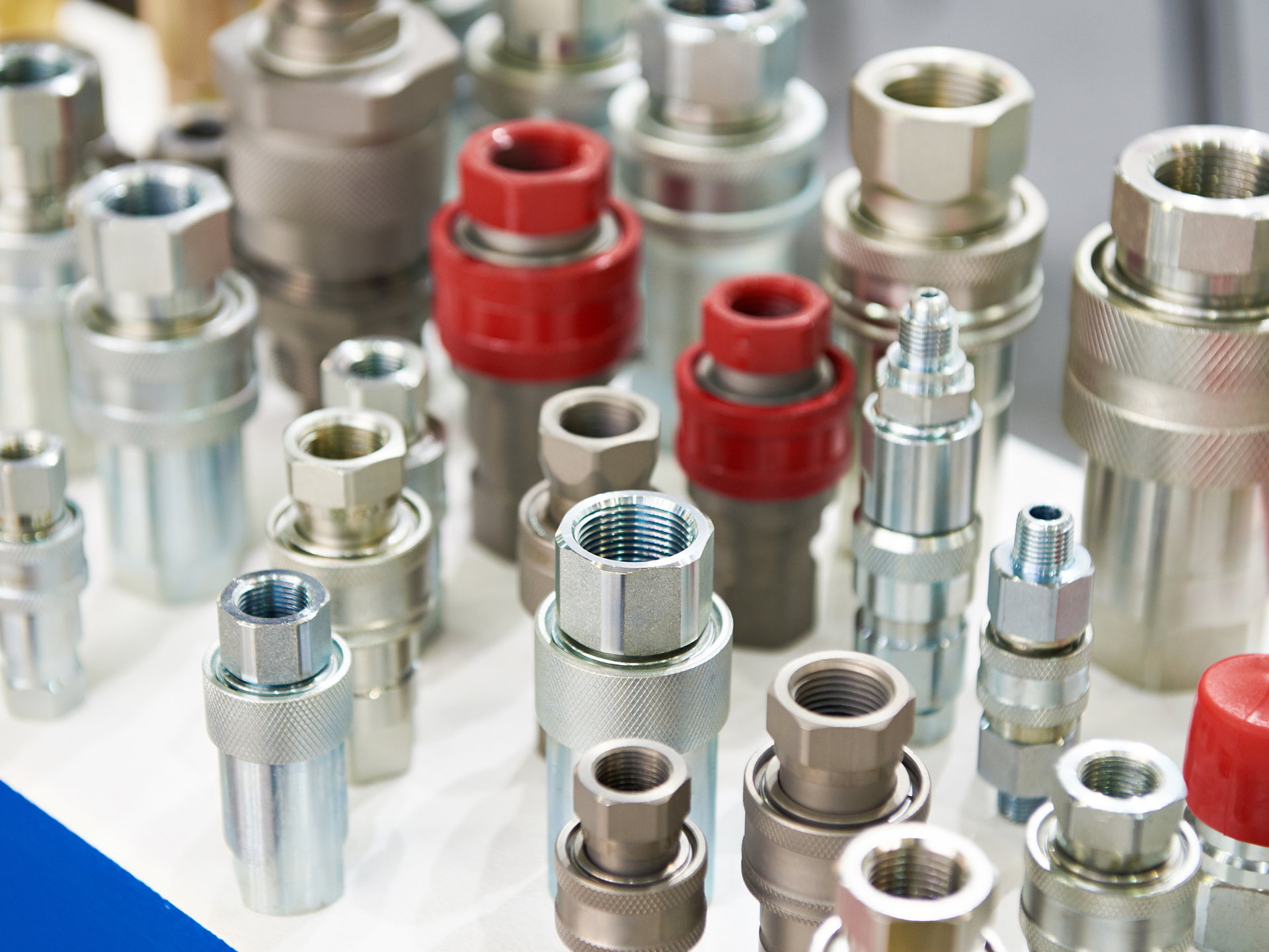 Close-up of various metal quick-connect hydraulic fittings, some with red or black caps, arranged on a surface.