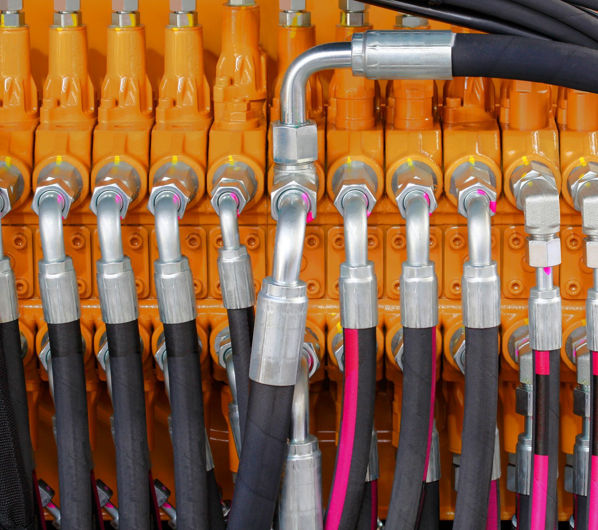 Close-up of orange hydraulic valves with silver connectors and black hoses.