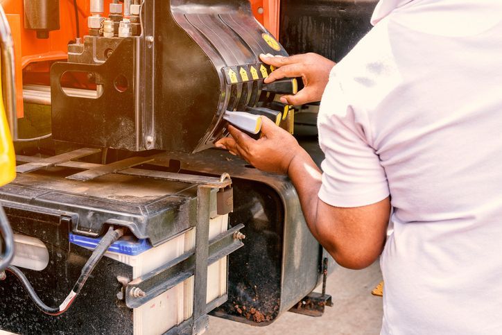 Technician inspecting hydraulic hose assemblies on heavy machinery during maintenance work.