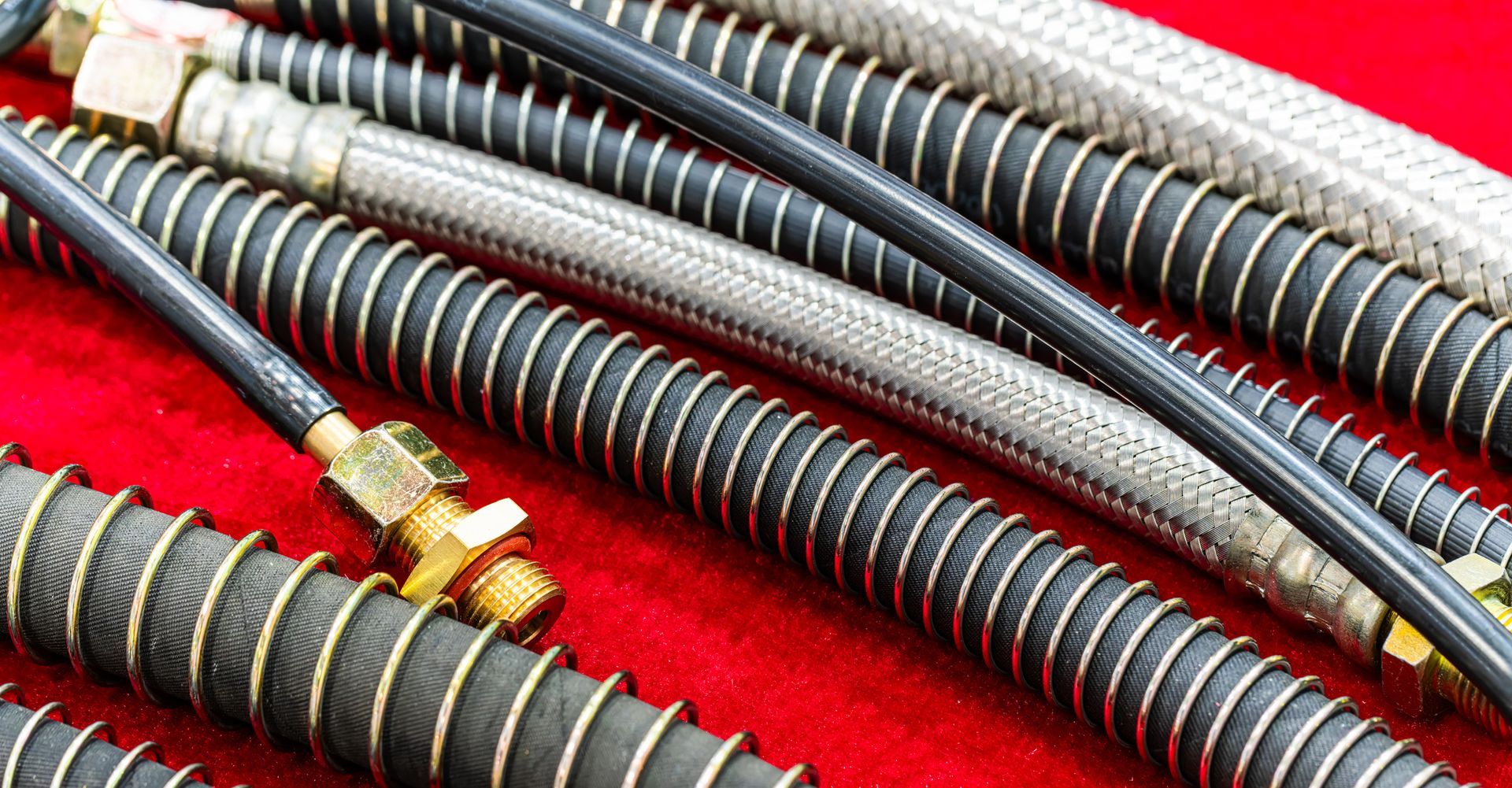 Close-up of various flexible hoses with metal braided and black corrugated exteriors, some with brass fittings.