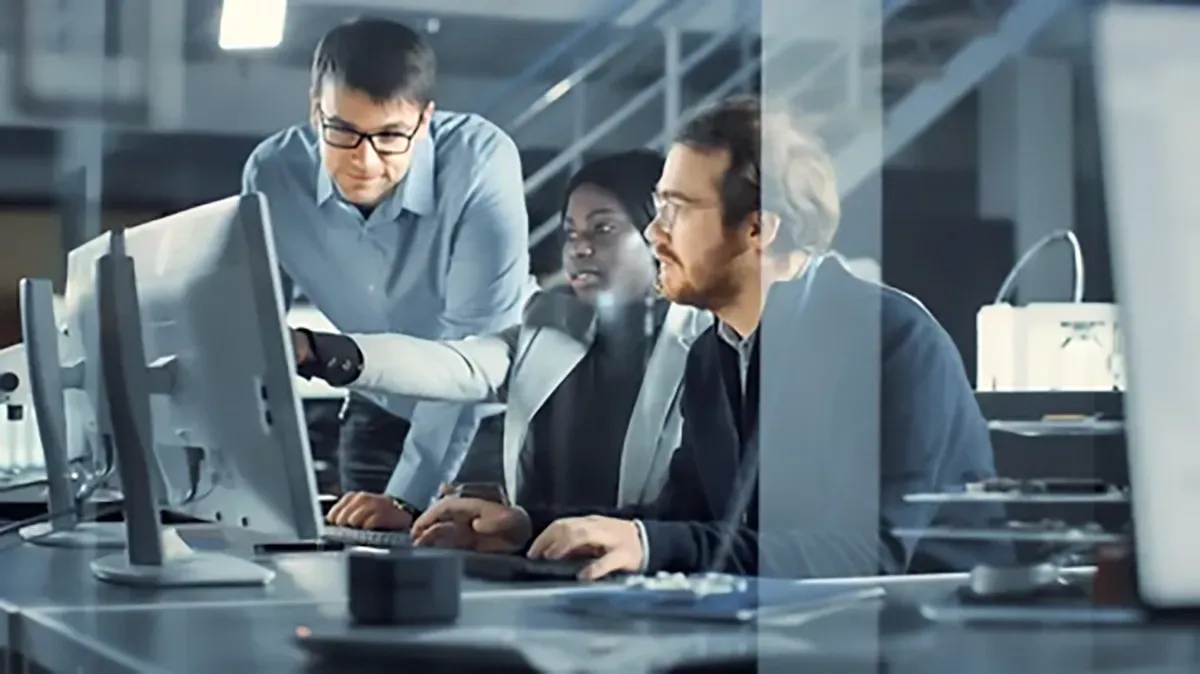 Three people collaborating at computers in an office setting.