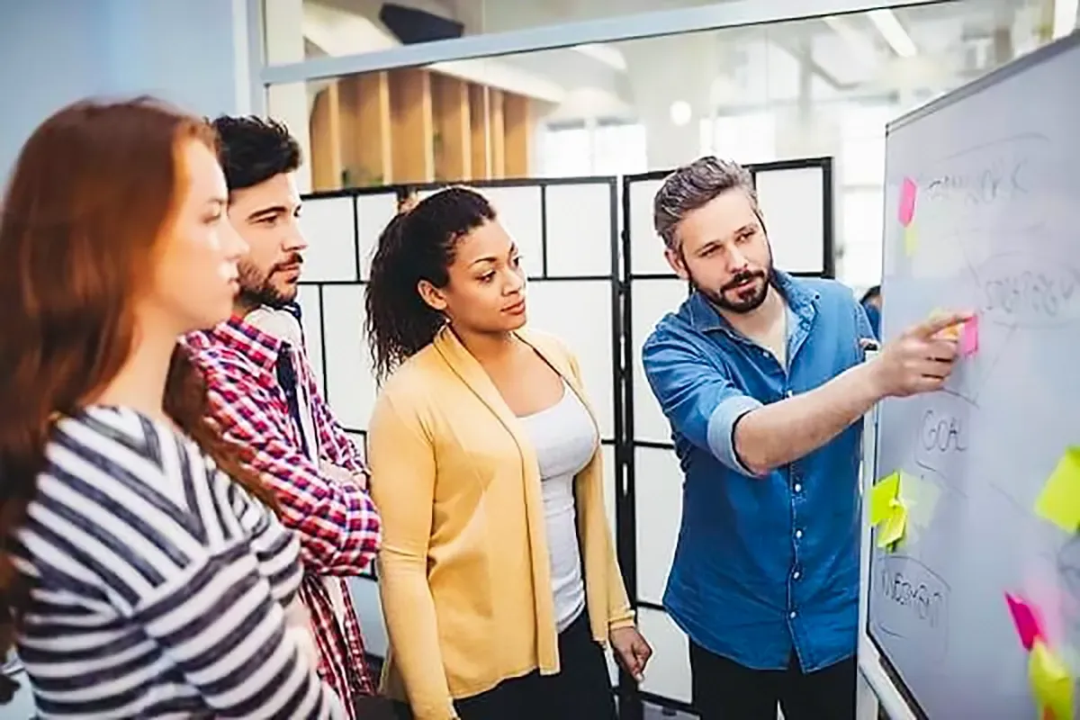 Group of people collaborating around a whiteboard with sticky notes in an office setting.