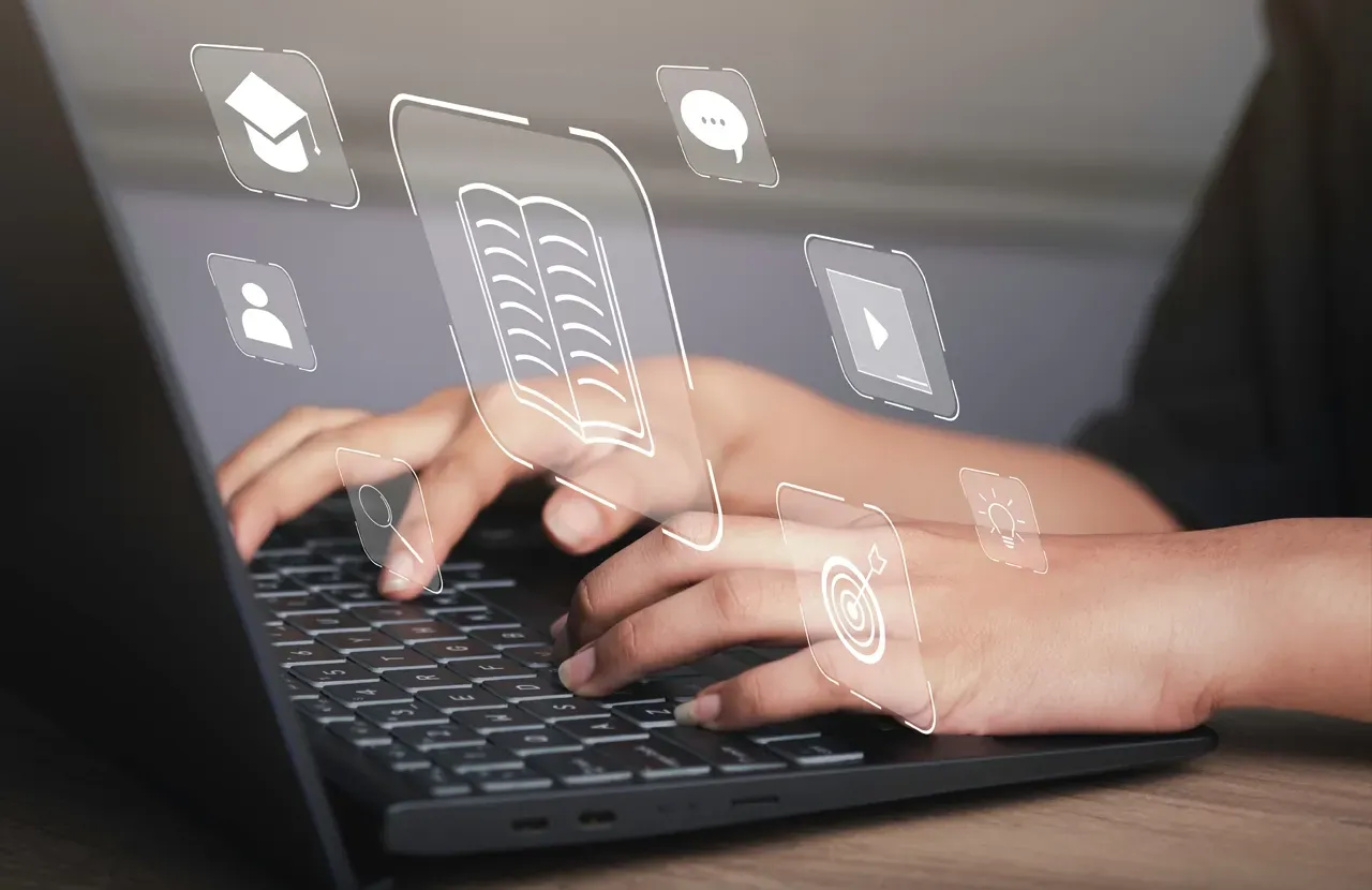 Hands typing on a laptop surrounded by glowing digital icons representing education, communication, and media.