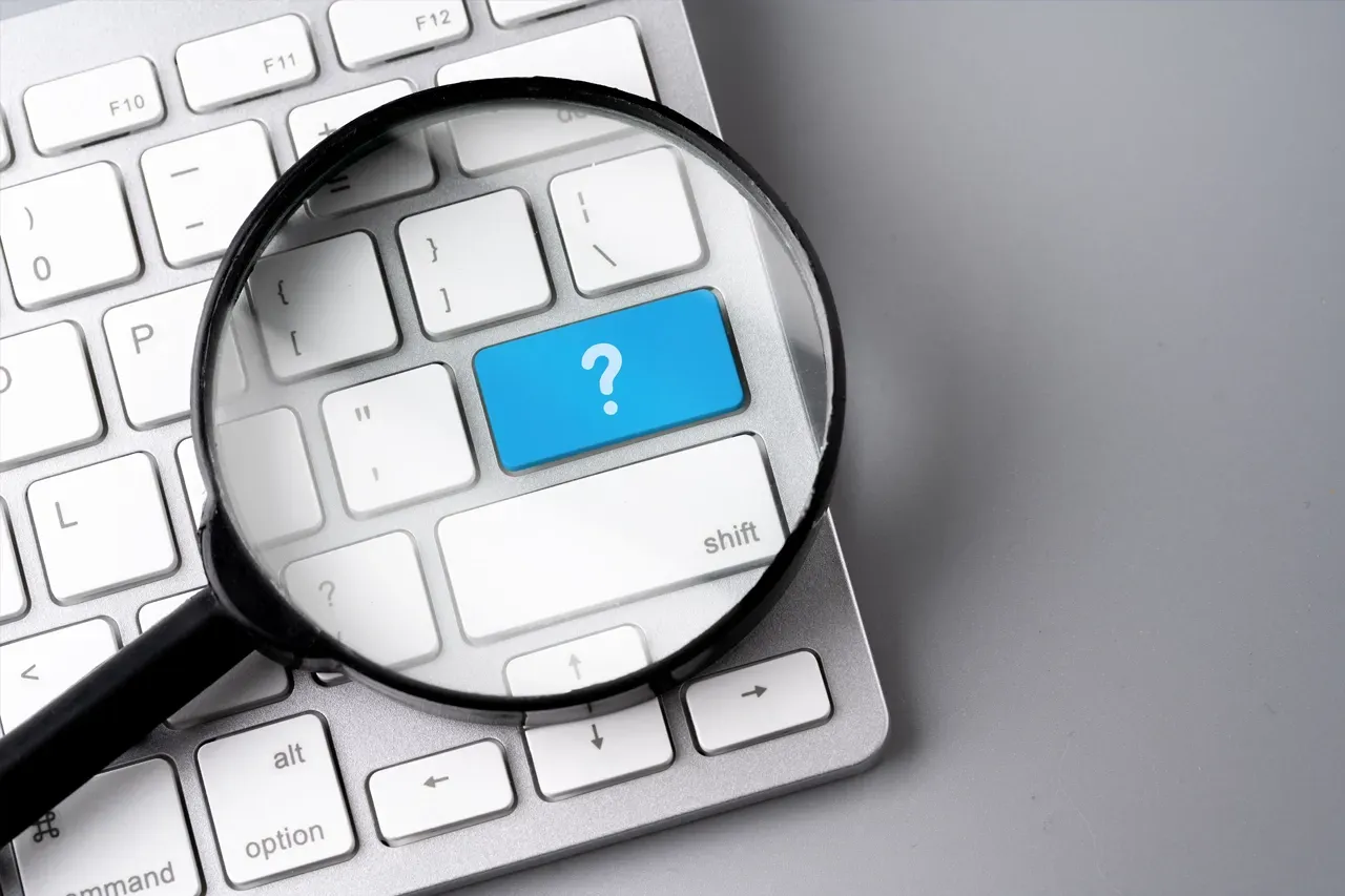 A magnifying glass is positioned over a white computer keyboard, highlighting a blue key marked with a white question mark.