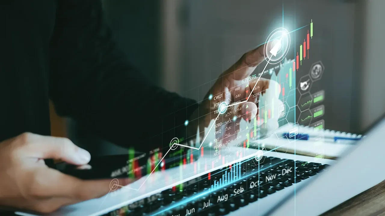 Hands interact with a laptop and smartphone surrounded by glowing, holographic financial stock market growth charts.