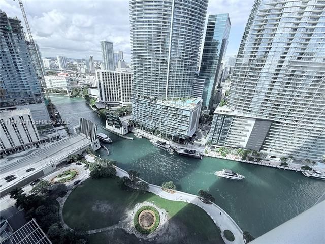 Aerial view of a river through downtown with tall glass skyscrapers and boats moving below