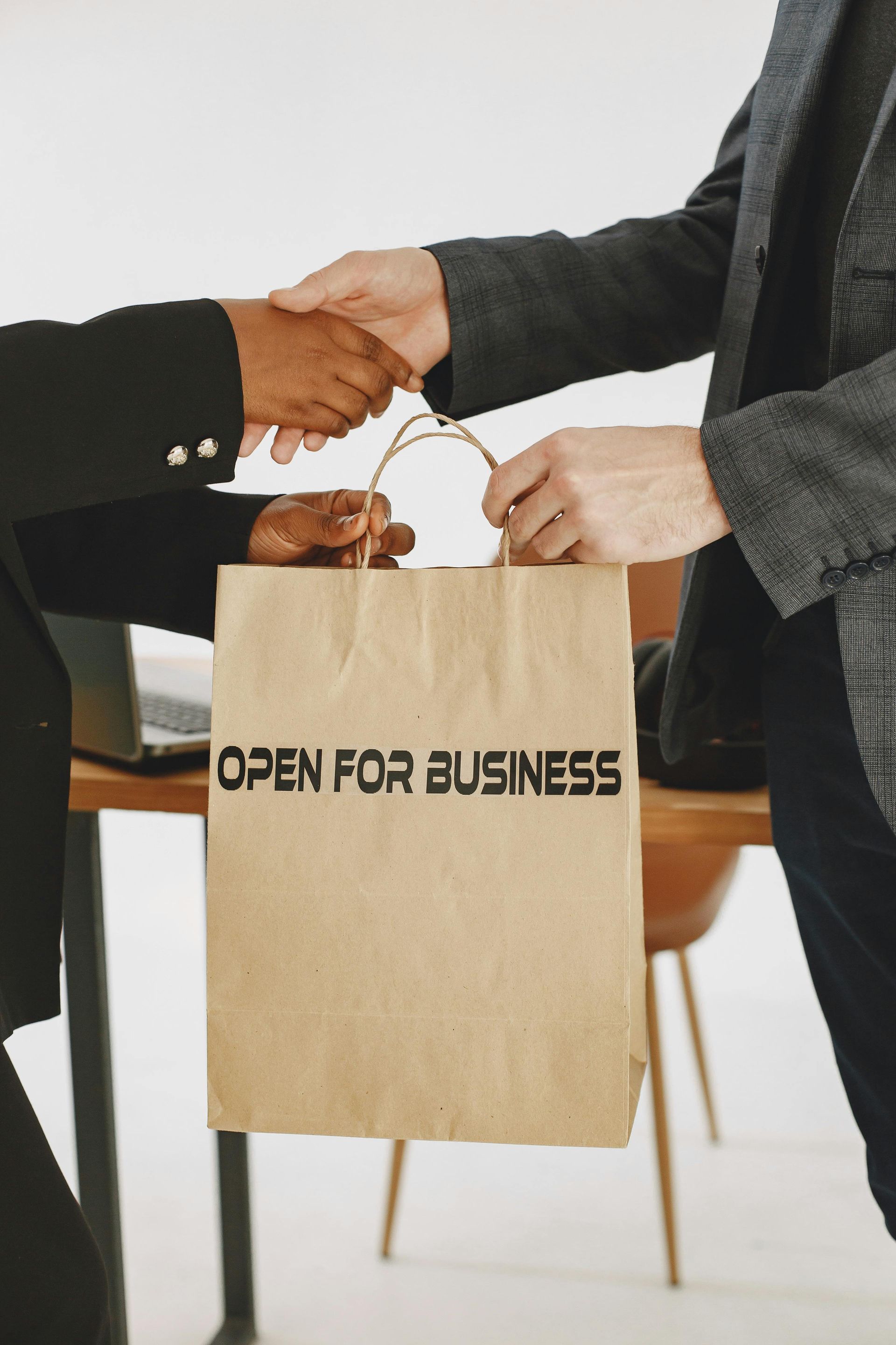 Two people shaking hands over a shopping bag labeled “OPEN FOR BUSINESS”