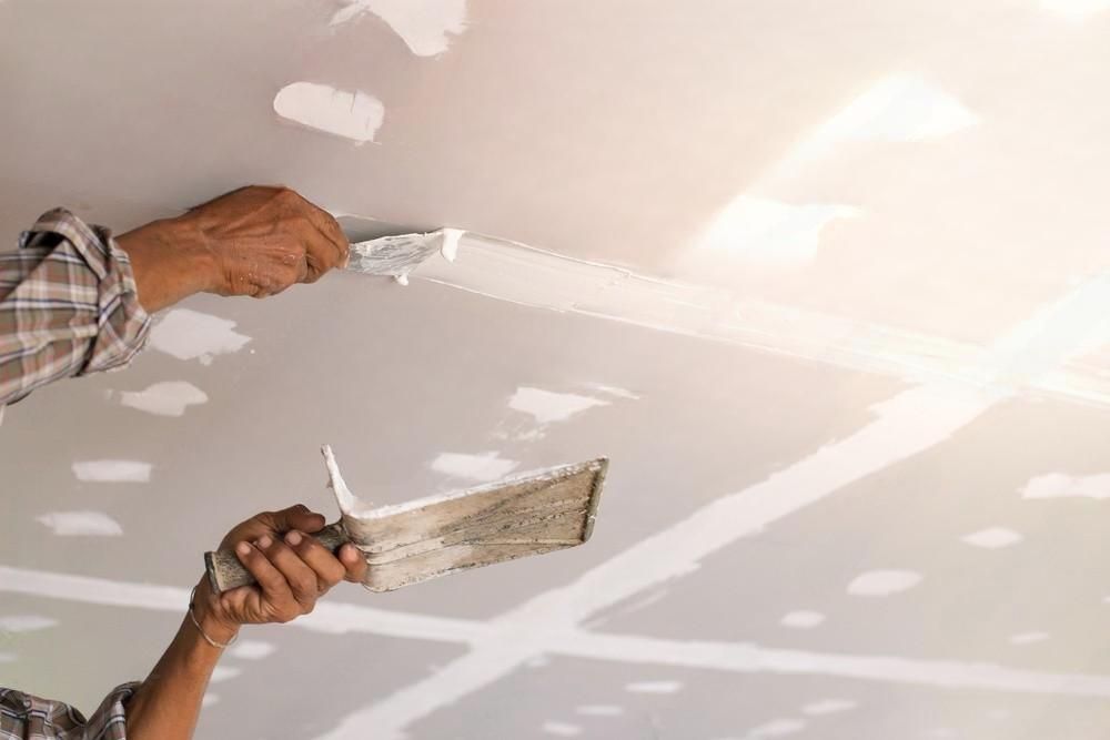 A man is plastering a ceiling with a trowel.