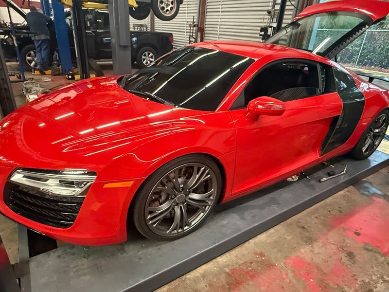 Red Audi R8 sports car in a garage with gullwing door open. Silver rims, tinted windows.