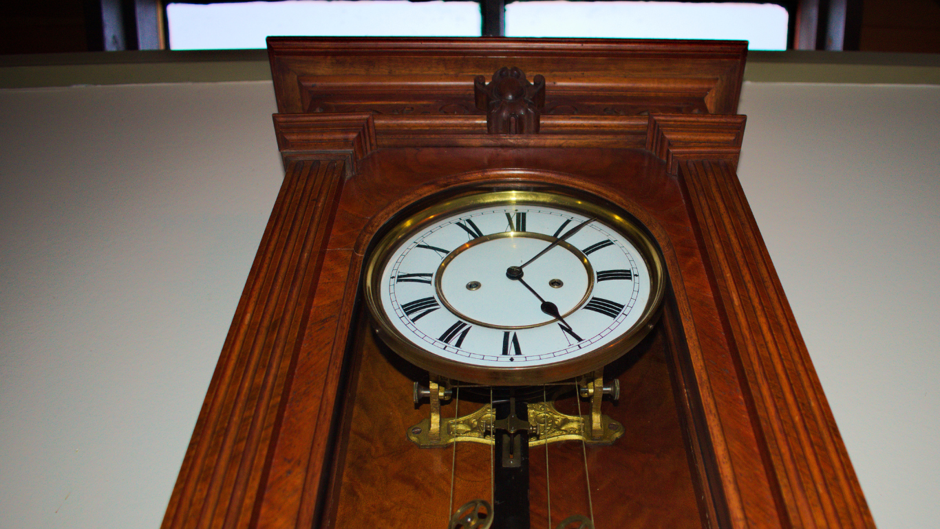 A wooden clock with roman numerals is hanging on a wall.