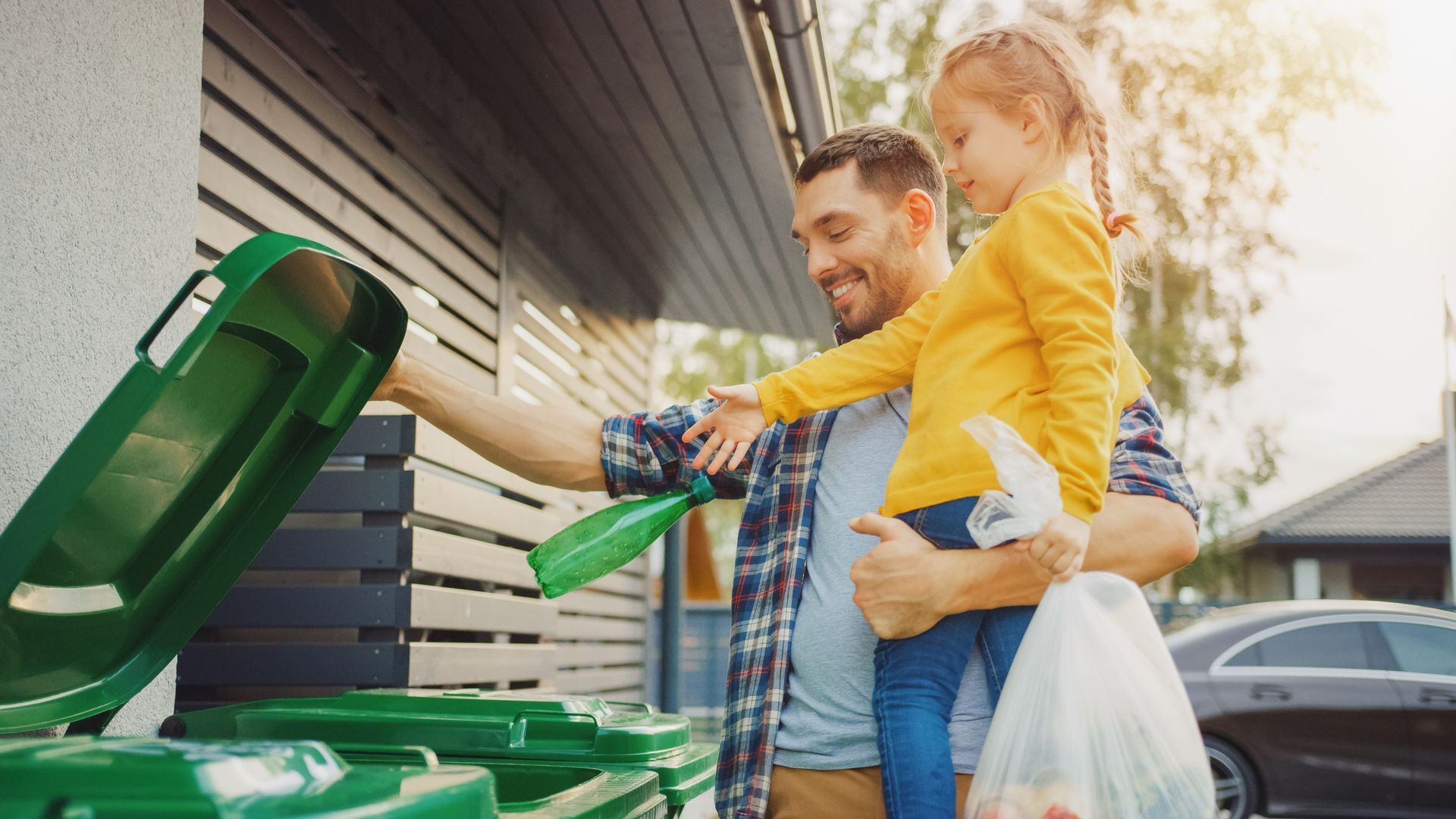 A man and a little girl are putting trash into a green trash can.