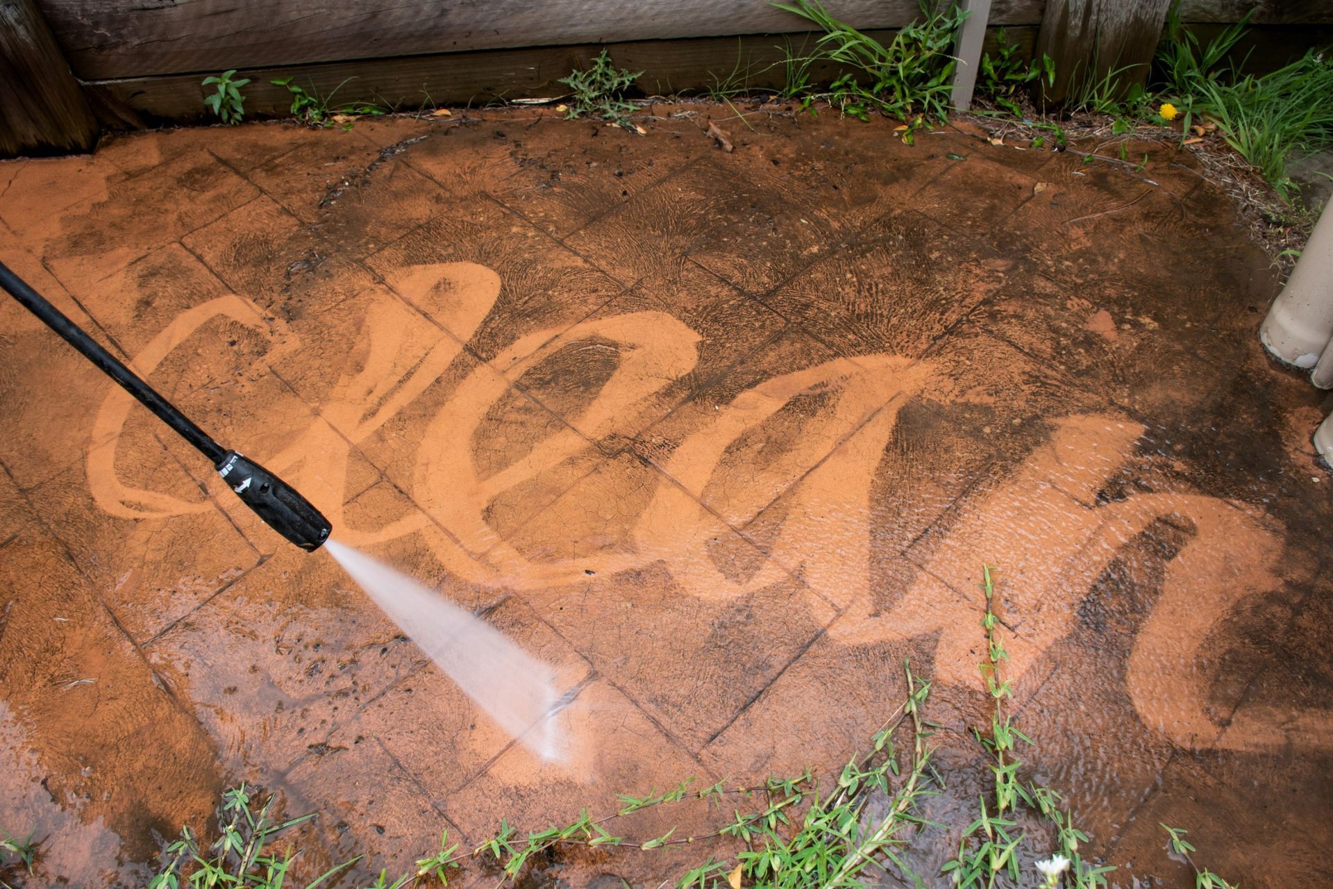 A person is using a high pressure washer to clean the word clean.
