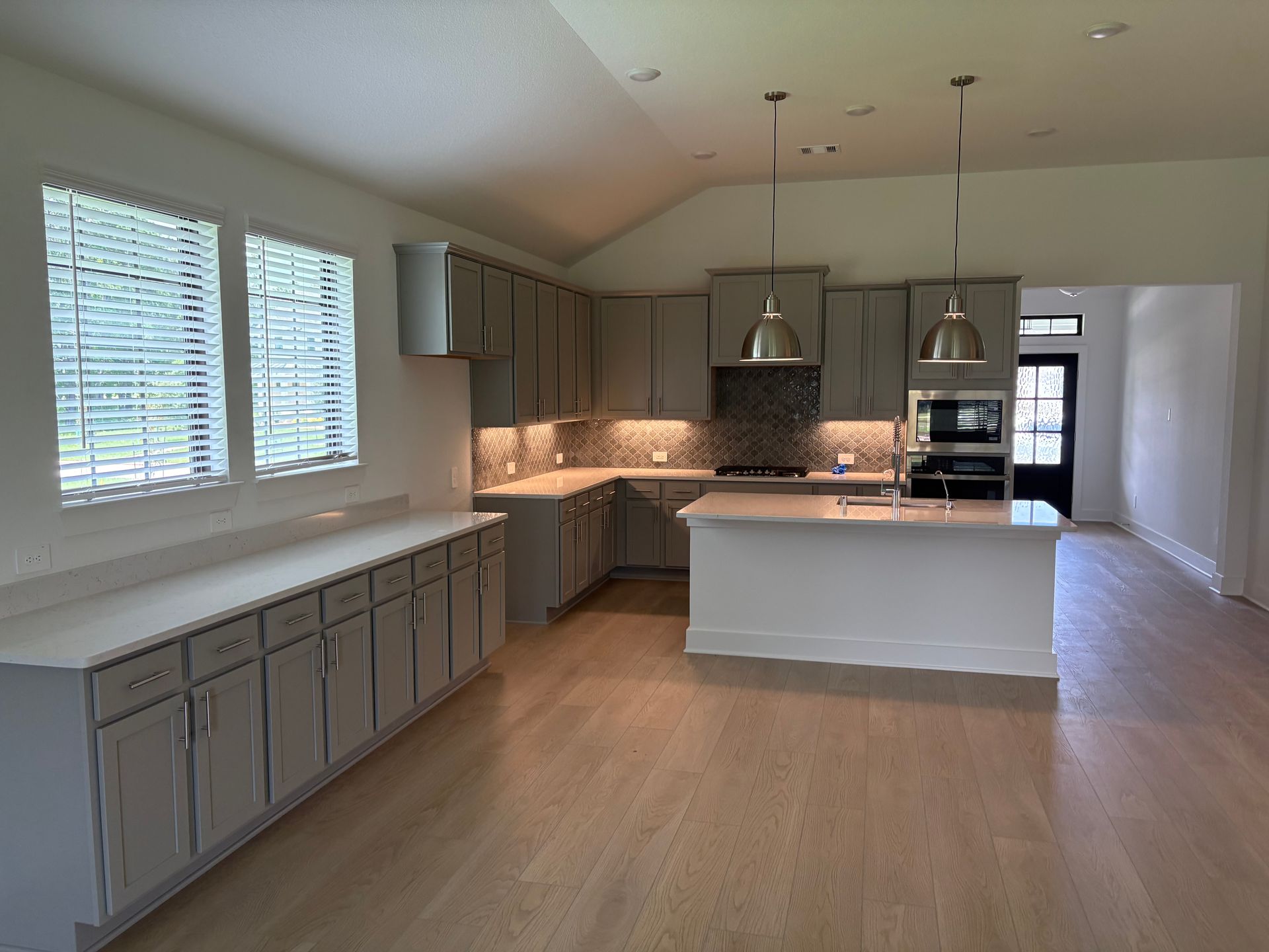 Kitchen with gray cabinets, white counters, stainless steel appliances, and light wood floors.