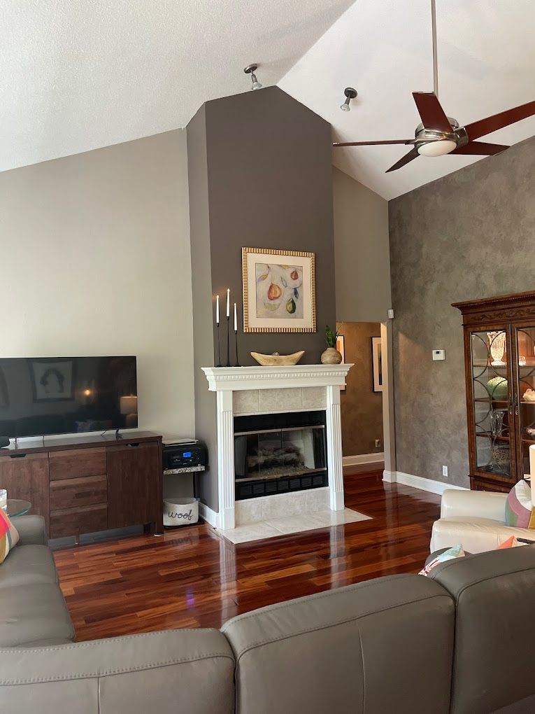 Living room with fireplace, TV, and brown leather couch. Dark gray accent wall, hardwood floors.
