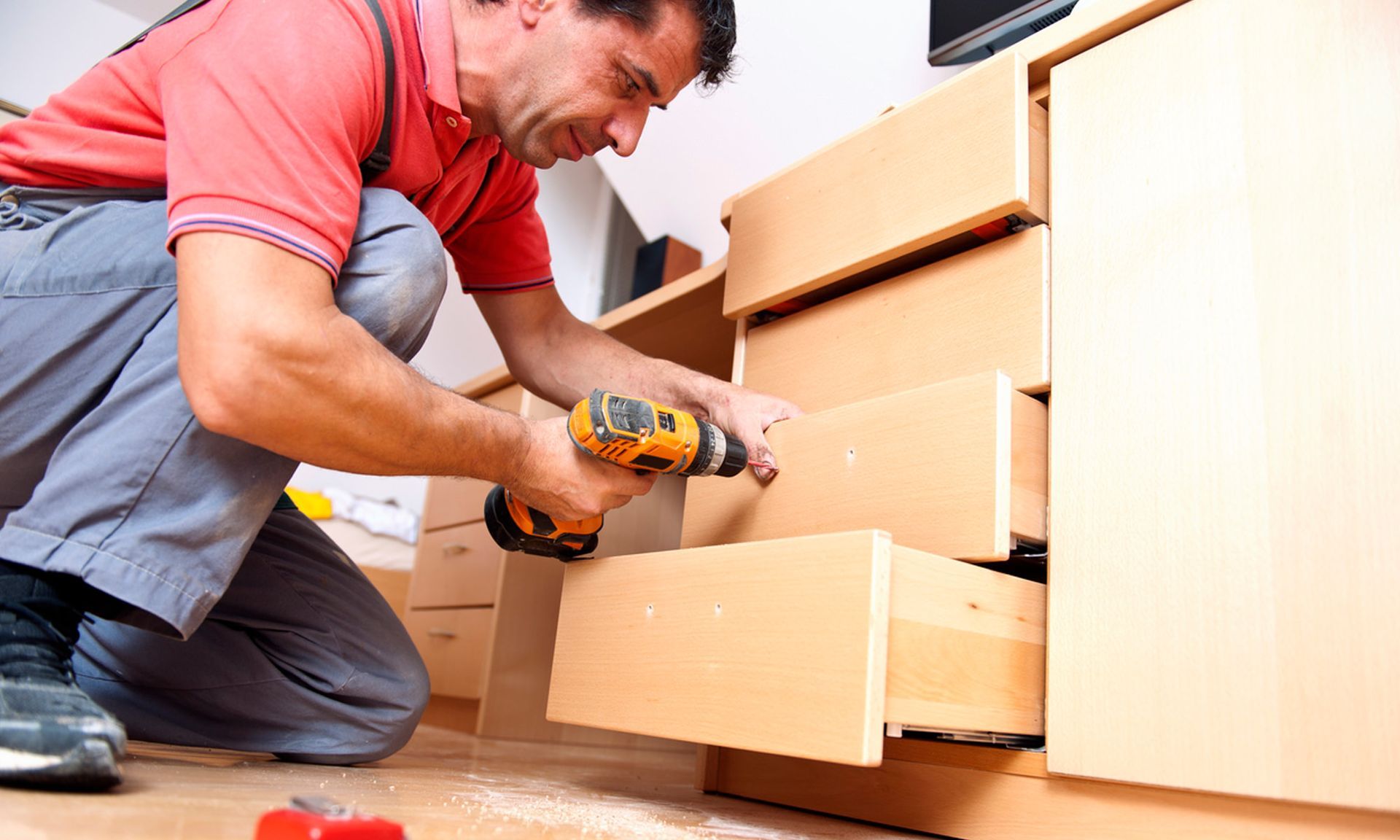 A man is using a drill to fix a drawer.