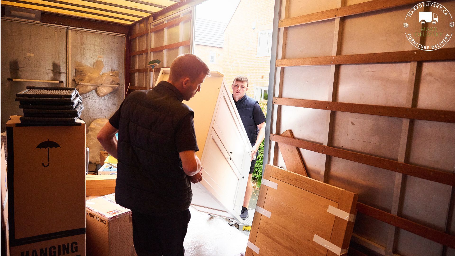 A man in a black shirt stands in front of a cardboard box that says hanging