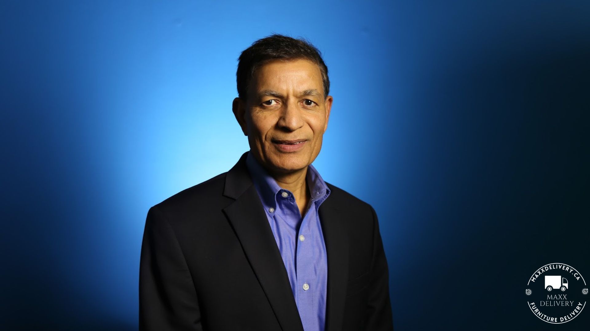 A man in a suit stands in front of a blue background