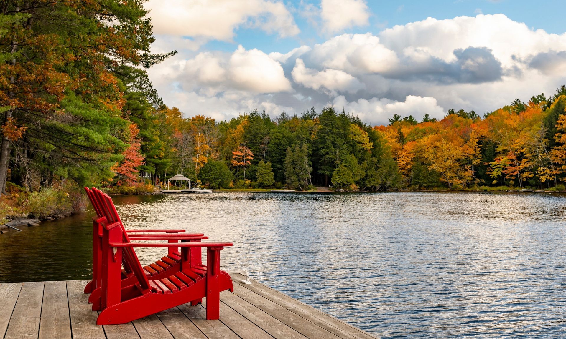 Two red chairs are sitting on a dock next to a lake.