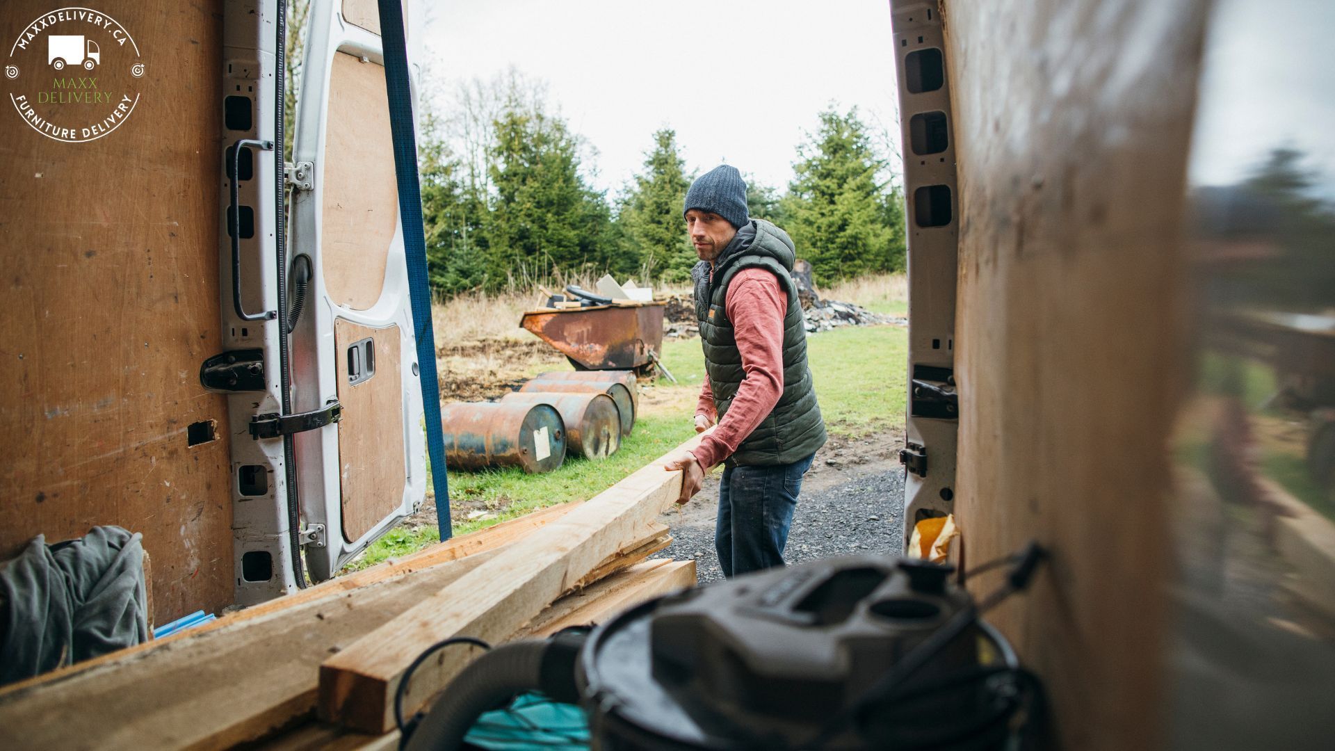 A man is standing in the back of a van holding a piece of wood