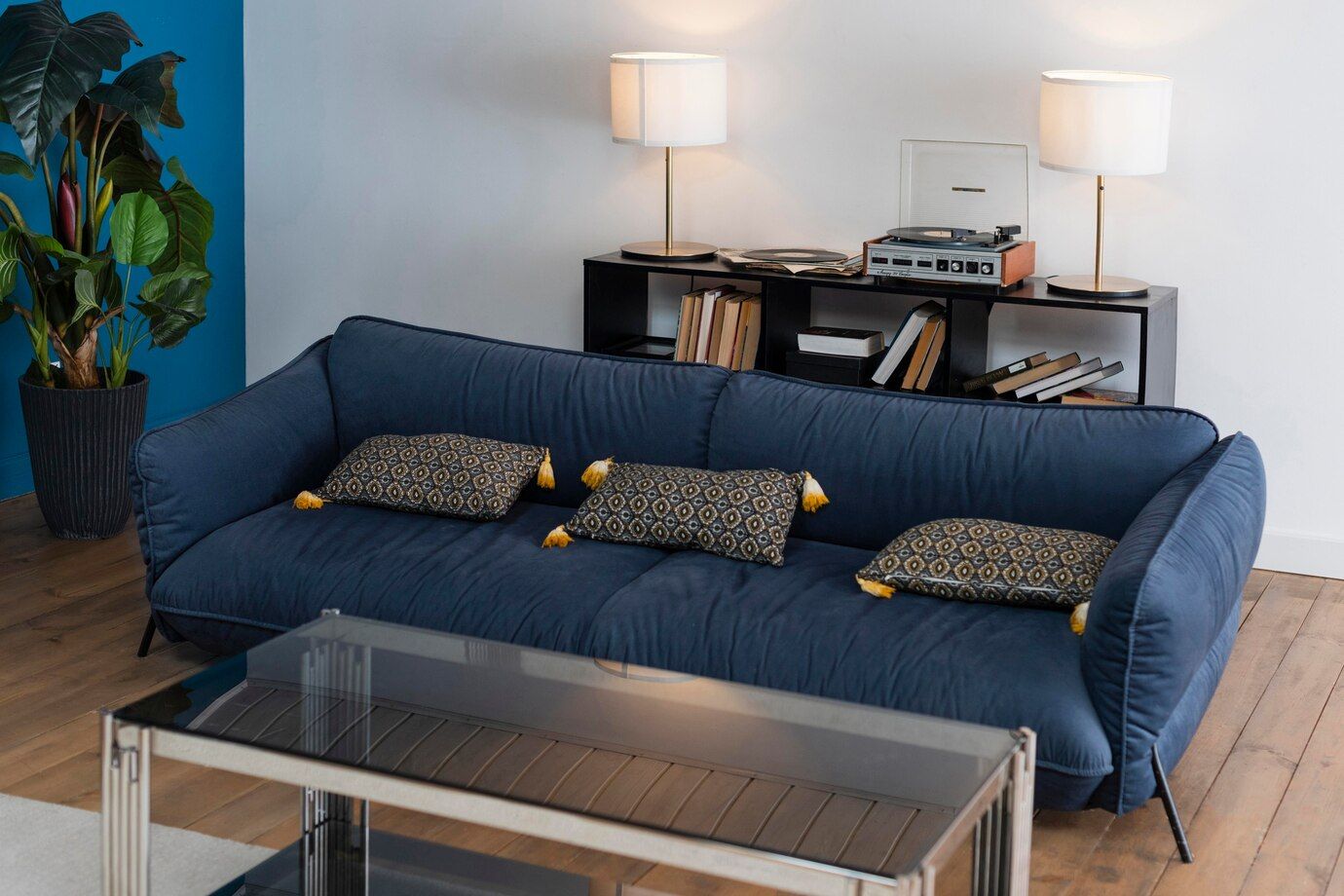 A living room with a blue couch and a glass coffee table