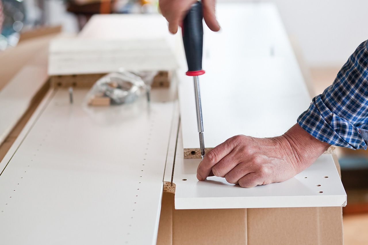 A man is using a screwdriver to drill a hole in a piece of wood - Funiture assembly services