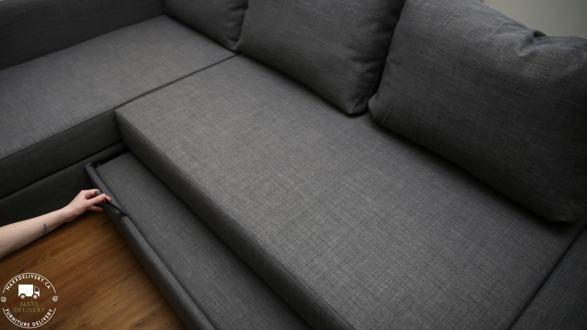 A person is opening a drawer on a grey sectional couch