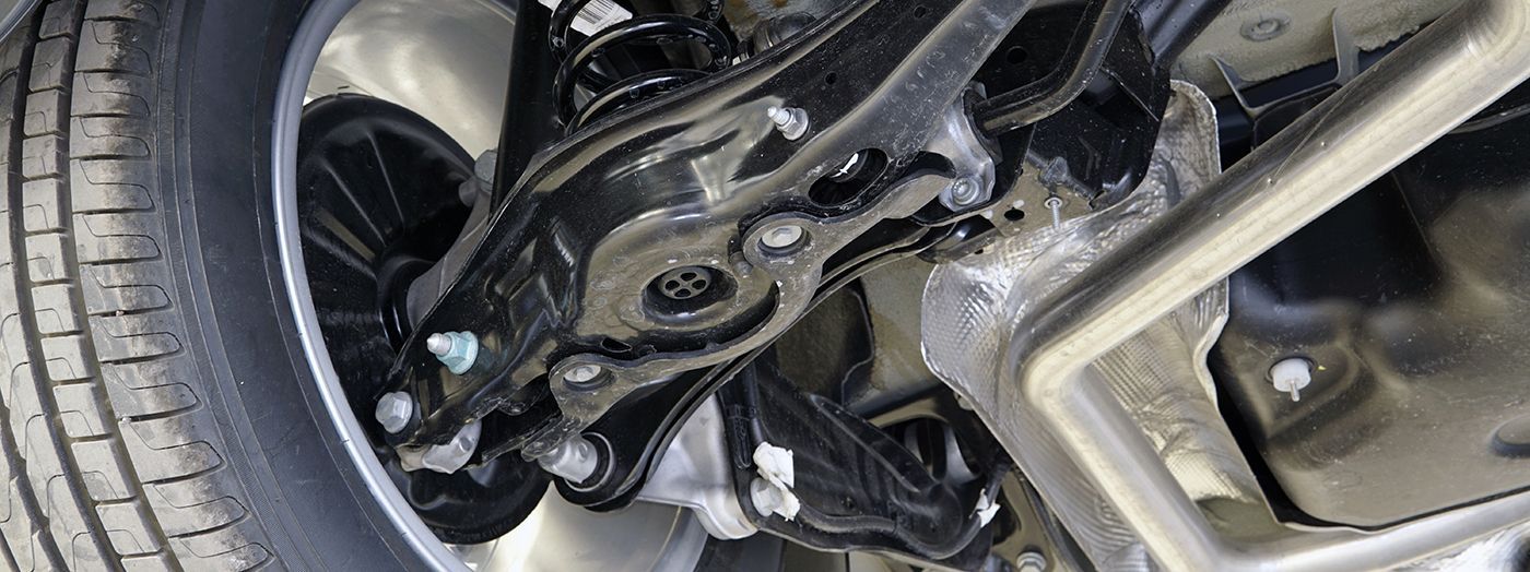 Underside of a car's rear suspension, showing black components, a tire, and metal bracing.