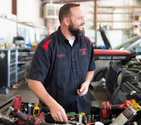 Mechanic smiling at work in auto repair shop, looking at toolbox.