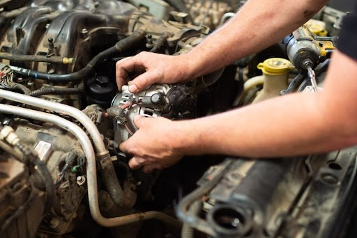 Mechanic working on a car engine, hands on an alternator.