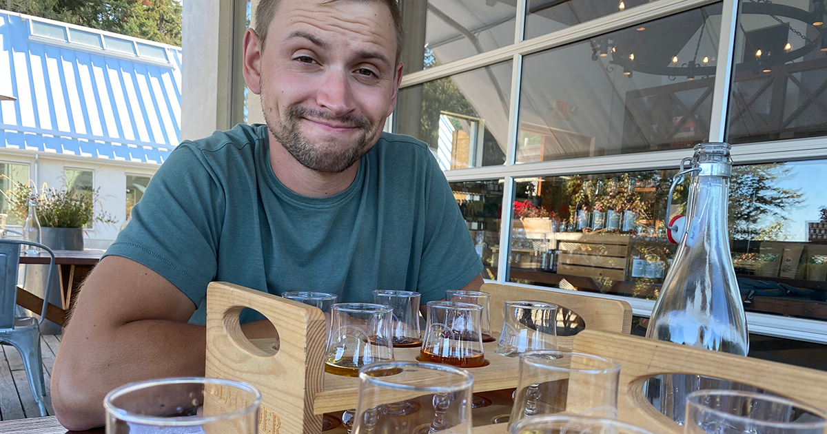 Bryce smiling while seated and enjoying a flight of craft brews.