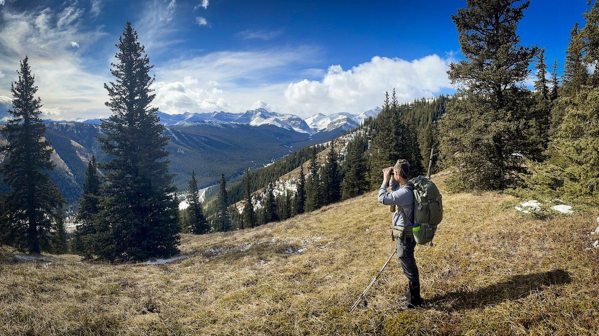 Sheldon in the mountains looking at the landscape through binoculars.