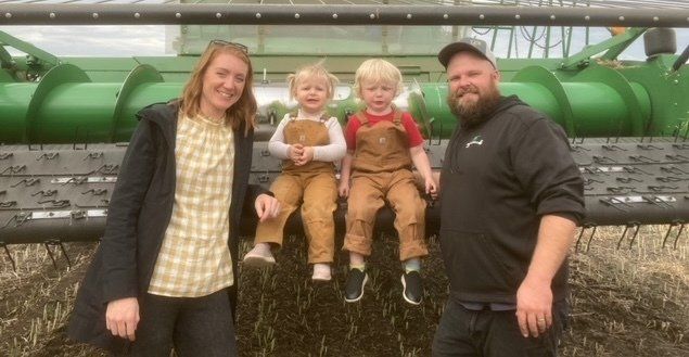 Dylan Graff, his wife and two children pose for a photo in front of their green combine.