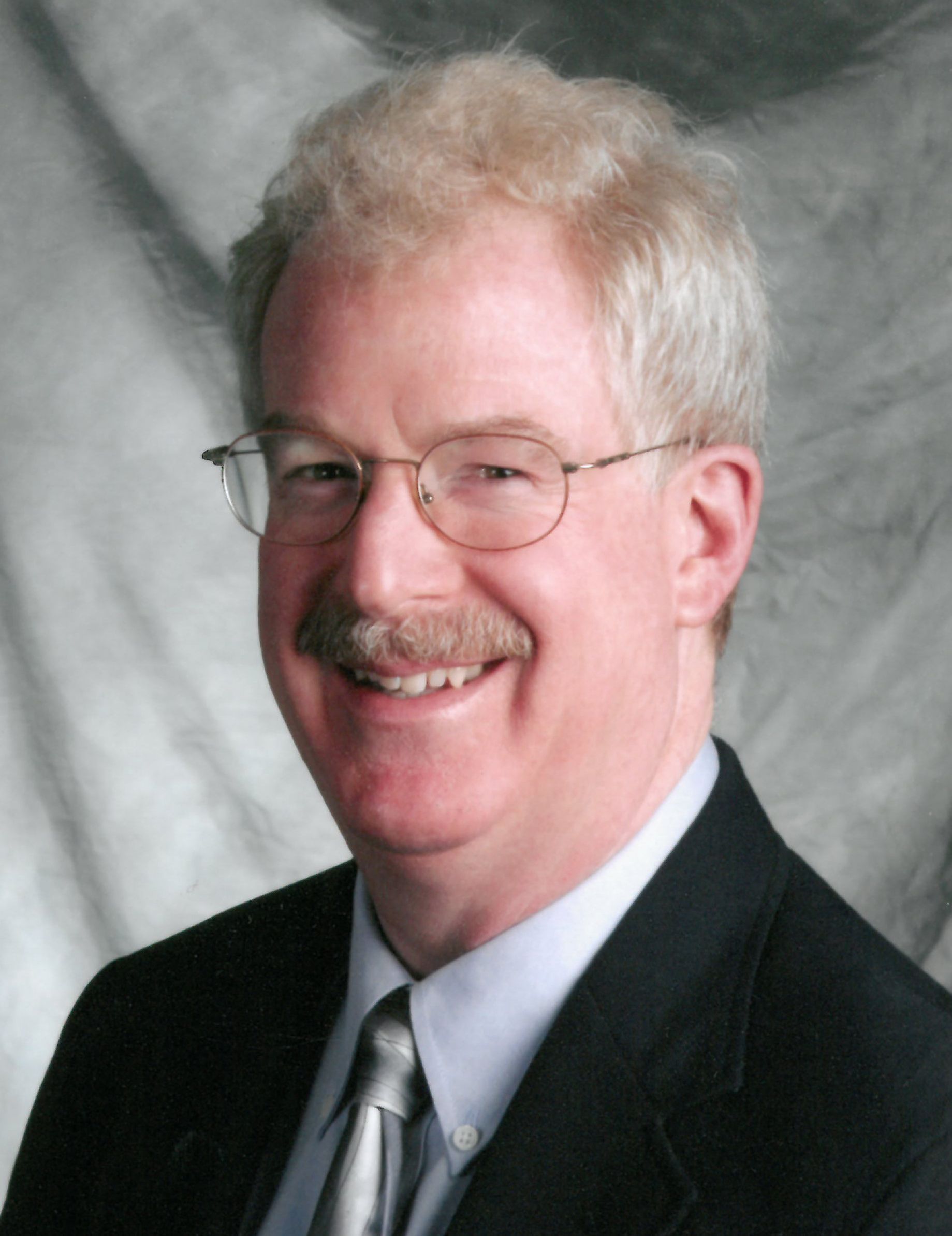 Portrait of a smiling person with glasses and dark hair against a light background