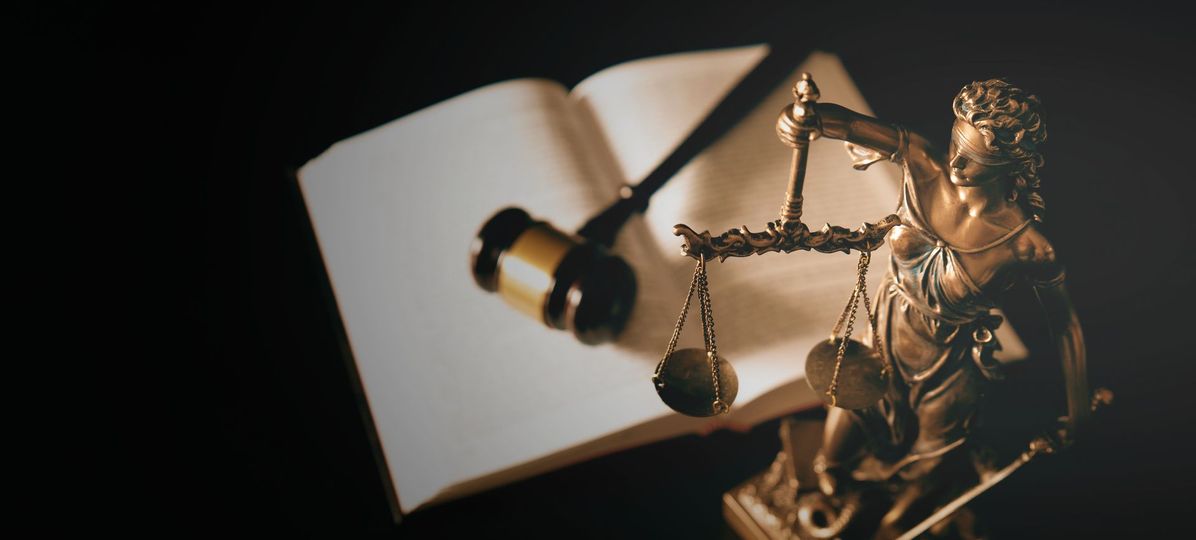 A statue of justice holding a scale and a gavel next to an open book.