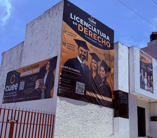 Un gran edificio con una bandera en la parte superior está rodeado de árboles.