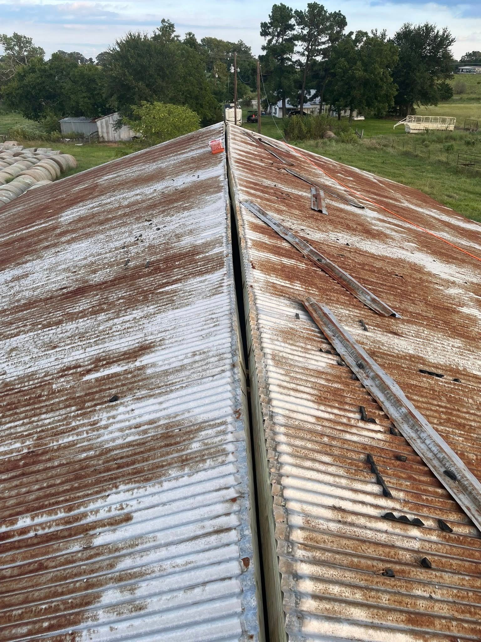 Rusty metal roof of a building with a center seam; rural setting with trees in the background.