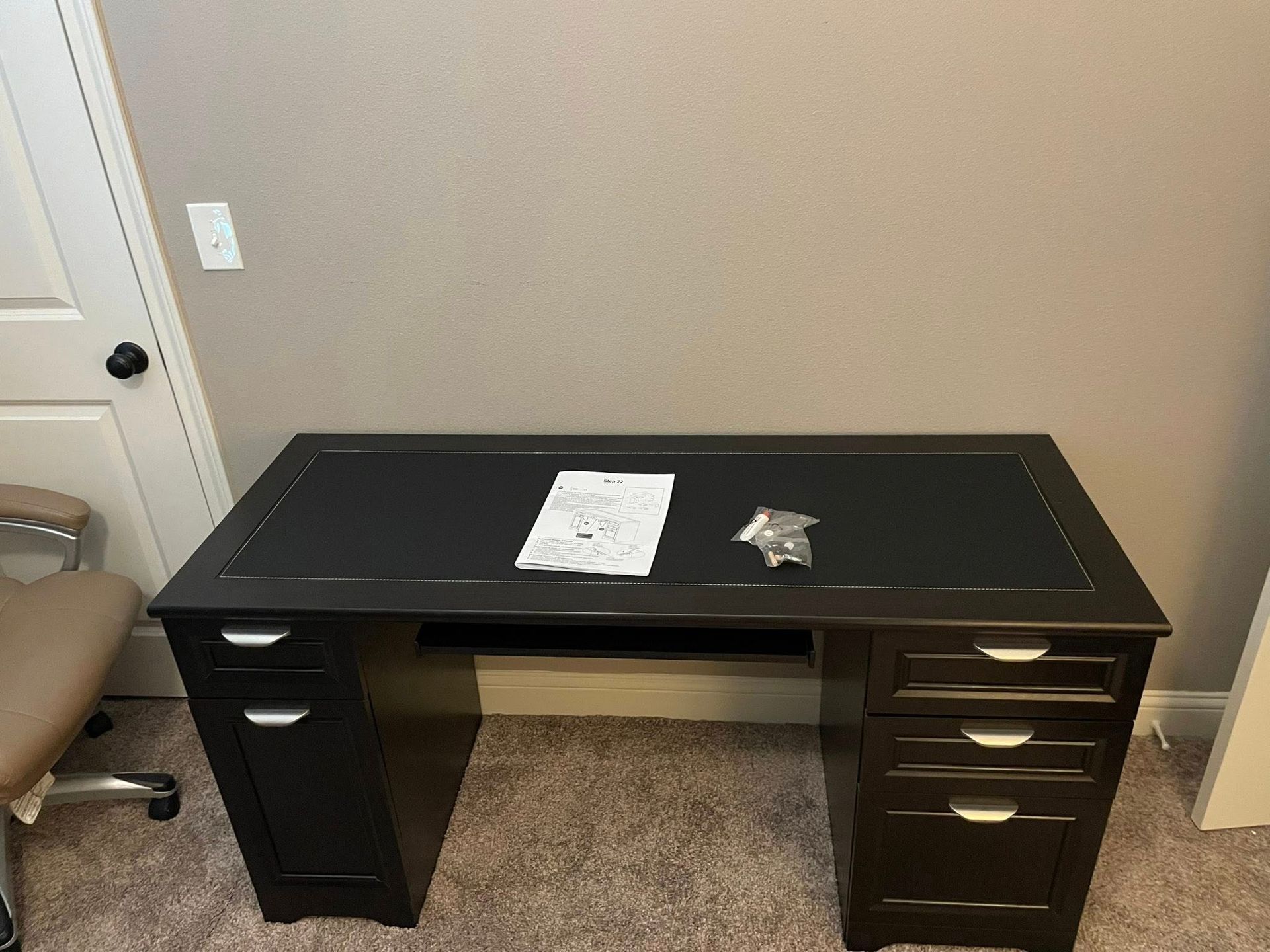Black desk with drawers, papers and hardware on top, in front of a wall.