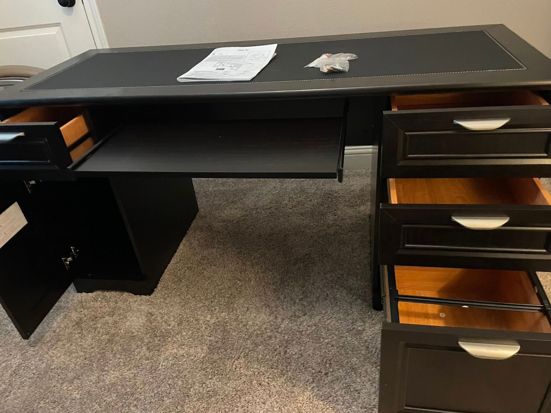 Black desk with open drawers and keyboard tray. Papers on the surface.