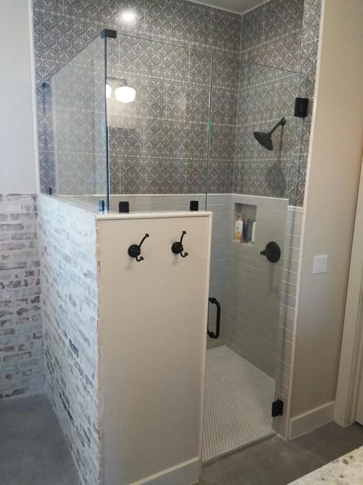 A bathroom with a walk in shower with a glass door and hooks on the wall.